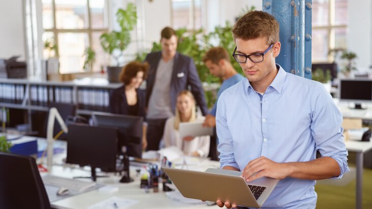 Ein Mann tippt auf seinem Laptop, während er in einem modernen Büro steht, ein Hinweis auf die steigende Nachfrage nach IT-Jobs in Fulda.