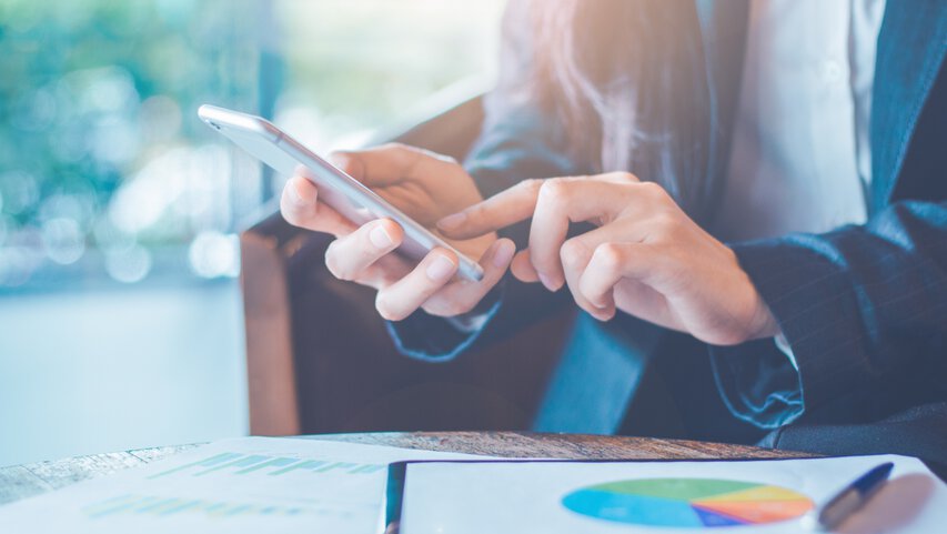 Mann sitzt am Laptop und hält ein Smartphone 