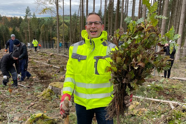 Ein Mann hält einen kleinen Baumsetzling in einem Wald – vielleicht Teil eines Projekts für Umwelttechnologien, die auch neue Jobs in Fulda schaffen können.