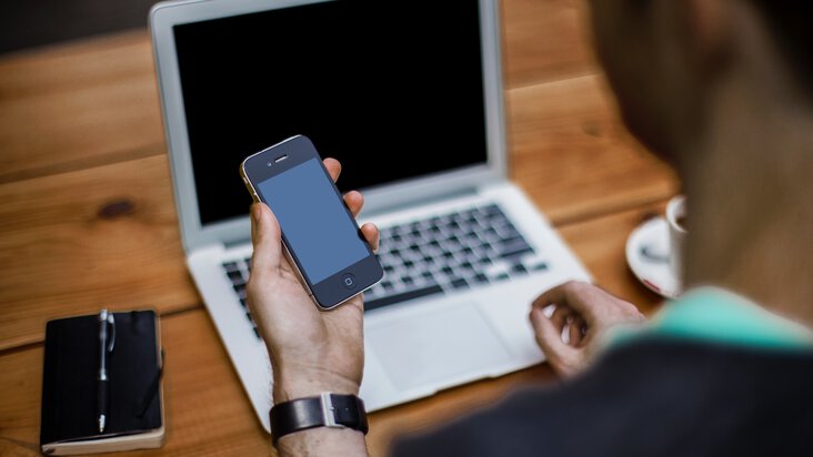 Mann vor dem Laptop hält Smartphone in der Hand 