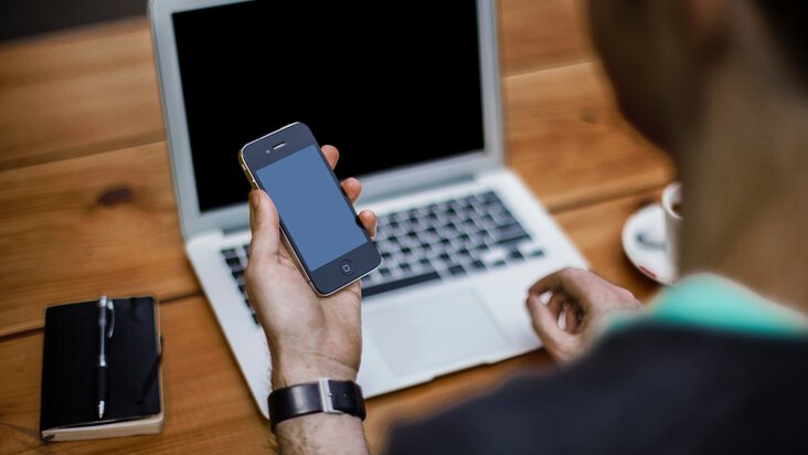 Un homme avec un smartphone devant un ordinateur portable